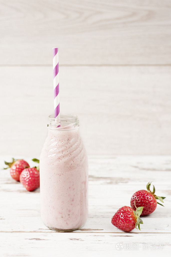 在玻璃瓶用稻草上旧的老式木制背景的草莓牛奶新鲜的草莓轻木表