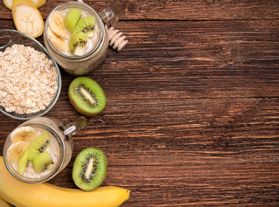 果汁与燕麦粉 香蕉 猕猴桃在玻璃瓶上木制的背景