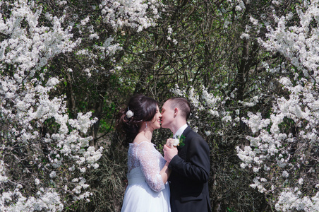 年轻的新娘和新郎在郁郁葱葱的花园在春天。新郎和新娘在花园里的白色连衣裙