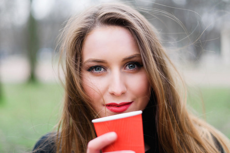年轻漂亮的时尚女孩在公园喝咖啡的肖像
