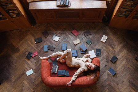 时尚的年轻女孩，在米色西装包围的书在红色沙发上看书。顶视图