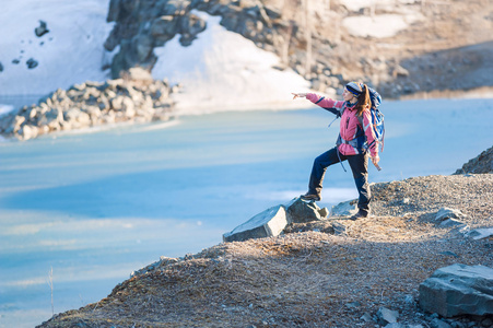一个背包的年轻女子指向结冰的湖岸上的距离