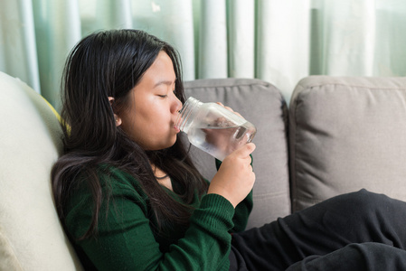 年轻漂亮的女孩在沙发上喝水