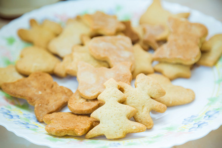 小女孩在厨房桌子上做饼干。在面粉中沾污的女孩。滚出面团和模子切开。面团。未煮的曲奇饼盘子里的成品饼干