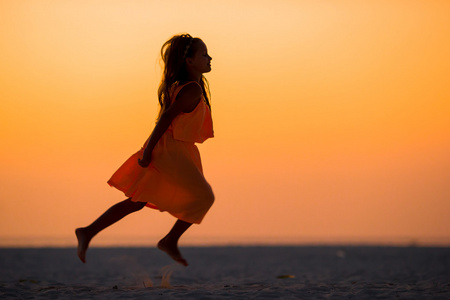 可爱的小女孩，在白色的海滩，在日落时的剪影