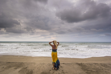 女孩站在砂海洋海滩上在多云的天气