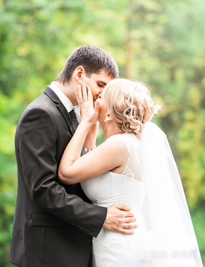 美丽的新婚夫妇在户外.他们亲吻和拥抱彼此