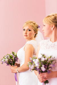 美丽的新娘金发女郎与白色婚纱礼服和发型明亮的妆看在镜子里