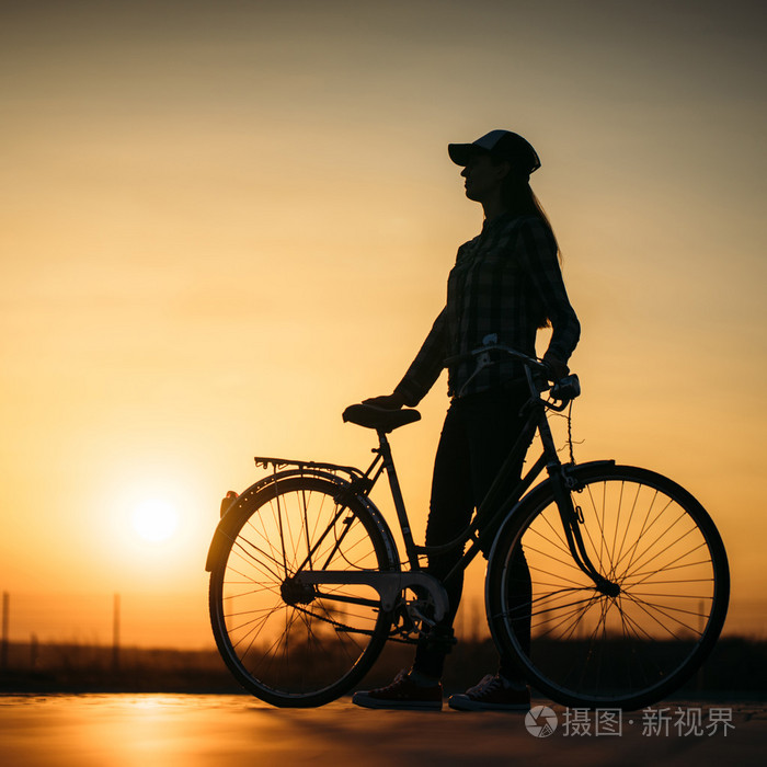 用一辆自行车在日落路上美丽时髦女孩