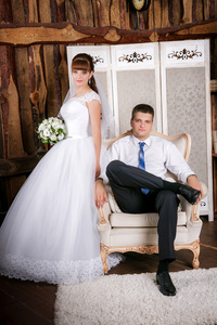 新郎坐在椅子上，新娘站在新郎在一个美丽的内部房附近