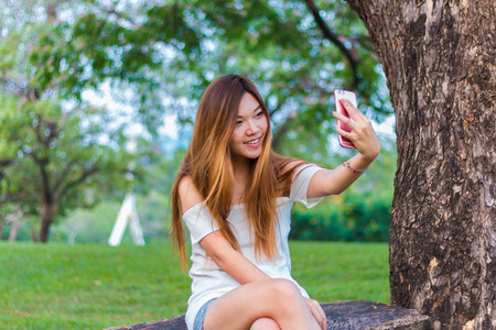 亚洲女人在花园或公园玩智能手机自拍照