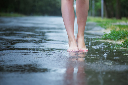 年轻漂亮的女孩在公园散步时在夏天暖雨中赤脚通过水坑有乐趣和享受
