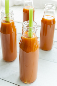 天然和新鲜的胡萝卜汁在小瓶里，在明亮的背景上新鲜西芹