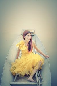 亚洲美丽的女人，在黄色的裙子坐在船上