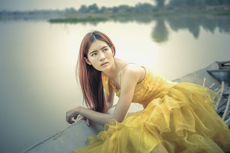 亚洲美丽的女人，在黄色的裙子坐在船上