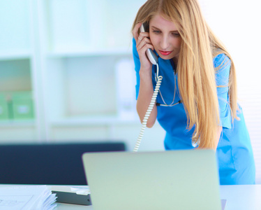 年轻的女医生穿白色上衣，在计算机上使用电话