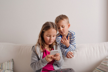 孩子们在家里坐在沙发上，玩智能手机