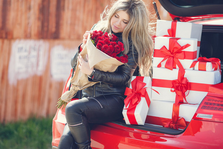 时尚的金发女郎，有着一束红玫瑰在汽车附近