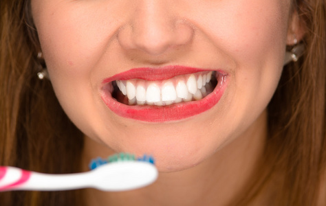 特写年轻女人口显示白色健康的牙齿和在前面拿着牙刷