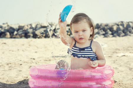 小女孩在玩在沙滩上，靠近海，在小的充气泳池