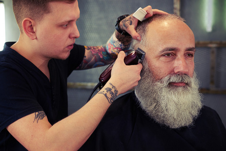 纹身向英俊时髦老人理发的理发师照片