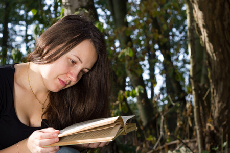 在巨大的森林里读一本有趣的书的漂亮年轻女孩