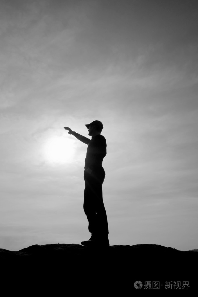 游客在触摸到太阳的徒步旅行者站在国家公园的砂岩岩峰上的红色棒球帽