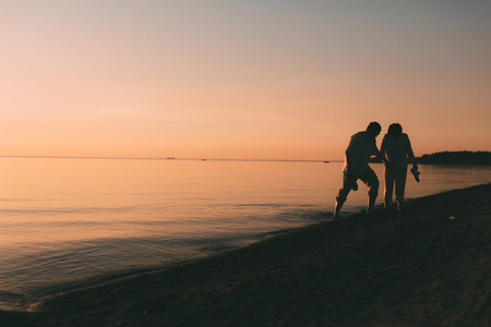 成人的夫妇站在反对日落海的剪影