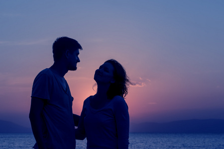 年轻夫妇站在海滩上享受日落。