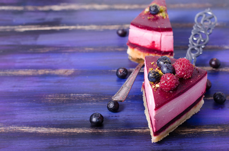 一块美味覆盆子蛋糕与新鲜树莓 蓝莓 黑醋栗和铲 明亮的紫色，紫色，蓝色背景上的开心果。可用空间为您的文字的