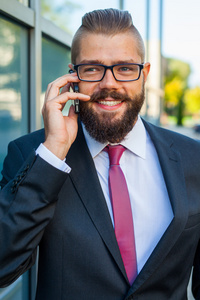 年轻胡子戴眼镜使用移动电话的商人