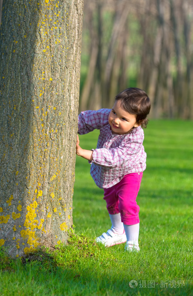躲在一棵树在森林后面的小女孩