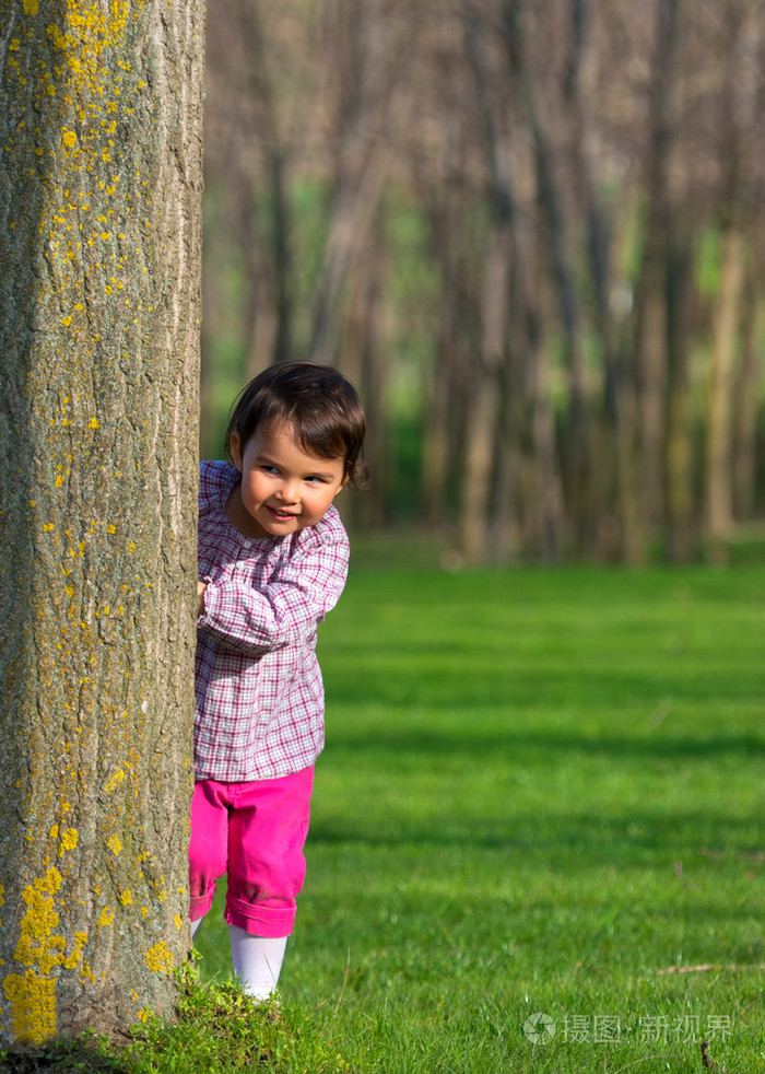 躲在一棵树在森林后面的小女孩