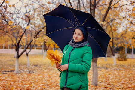 拿着树叶和雨伞的可爱年轻女人图片