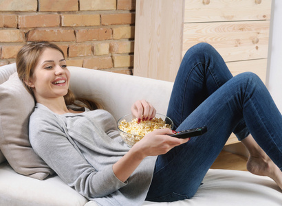 年轻女人放松和爆米花在沙发上看电视