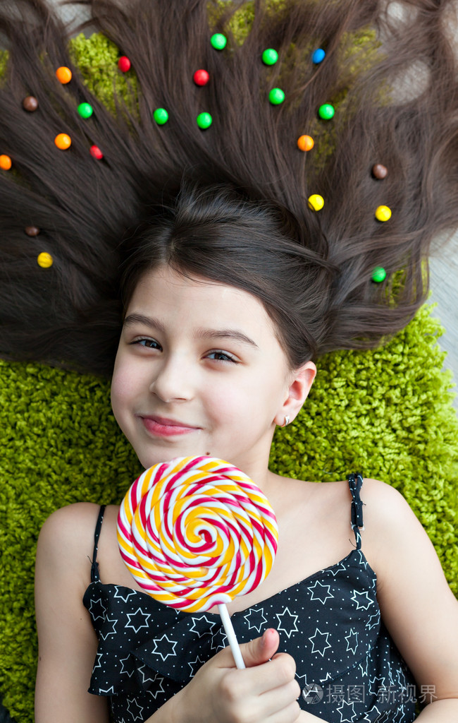 一个黑发的小女孩躺在地板上,躺在糖果中间.