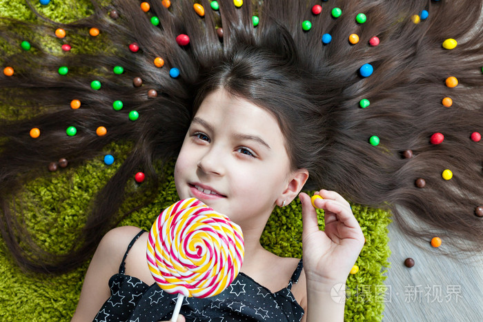 一个黑发的小女孩躺在地板上,躺在糖果中间.