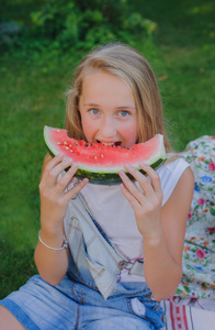 可爱的年轻女孩，在夏季在草地上吃西瓜