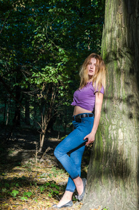 长长的金发，穿着牛仔裤和夹克在树林之中的树木和植被构成年轻美丽性感的女孩金发模型