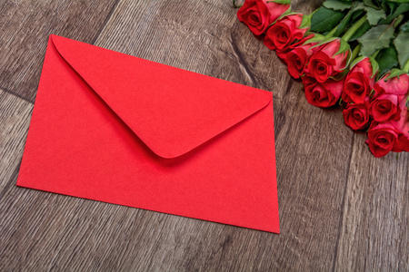 红色的信封和木制的背景上的玫瑰