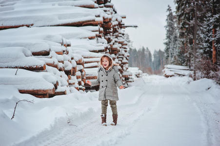可爱的快乐女孩肖像在冬天的森林里散步，背景上有树木砍伐