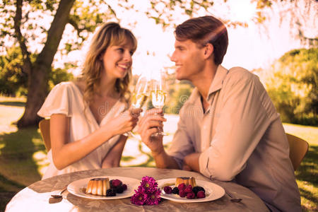 可爱幸福的情侣坐在外面用香槟和甜点敬酒