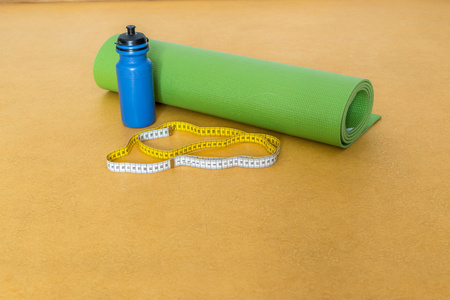 厘米磁带 瑜伽垫和瓶水为行使 onyellow 背景。瑜伽的设备