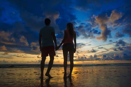 年轻夫妇手牵着手在海滩的爱在落日下的剪影