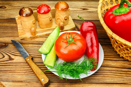 木桌上有番茄胡椒新鲜农产品蔬菜柳条篮和刀的盘子