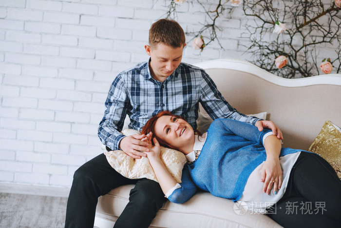 怀孕的年轻夫妇,在爱的沙发里.女人躺着的男子的膝盖.