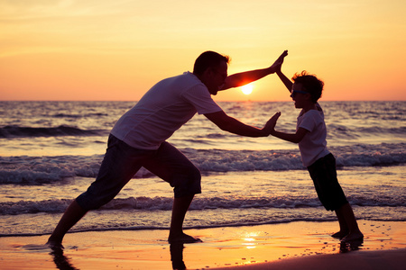 父亲和儿子在日落的时候在海滩上玩