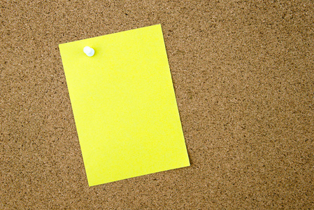 空白的黄色纸笔记寄托在软木板