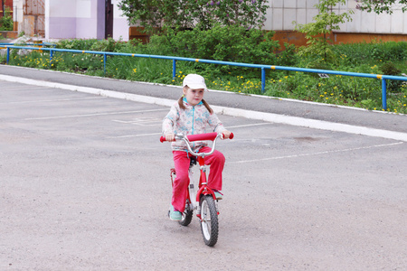 小可爱的女孩骑自行车在停车场附近的建筑