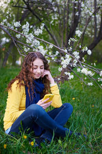 美丽的年轻女子坐在用智能手机的草地上